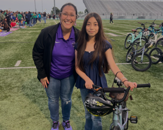 A smiling woman and a girl pose together with a bicycle on a green field.