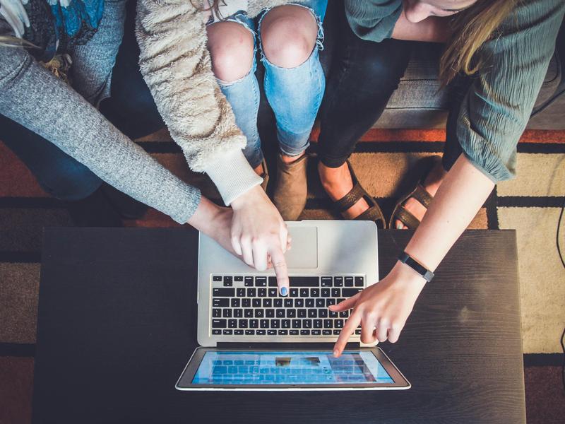 Three people collaborating over a laptop on a coffee table.