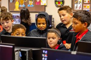 Group of children gathered around a computer screen, focused.