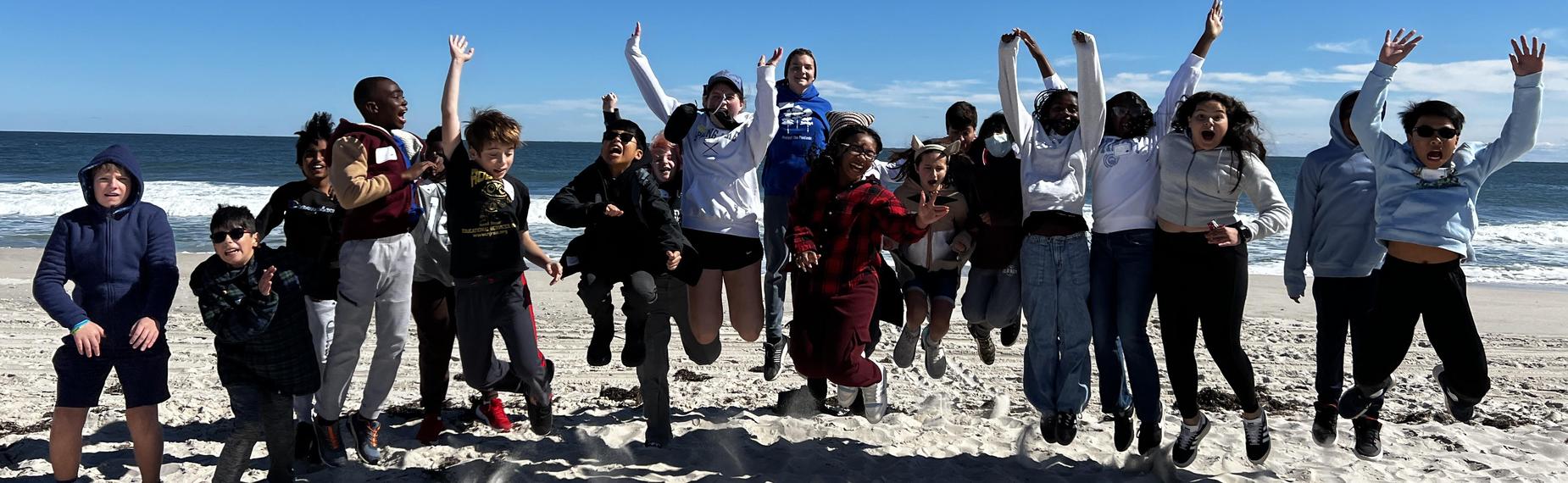 A group of children joyfully jumping on a beach with the ocean in the background.