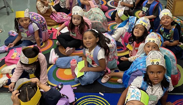 Students in paper hats on a rug in the classroom.