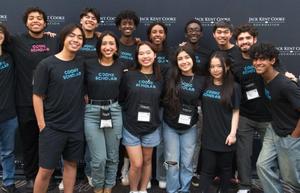 Group of smiling students wearing matching t-shirts at an event backdrop.