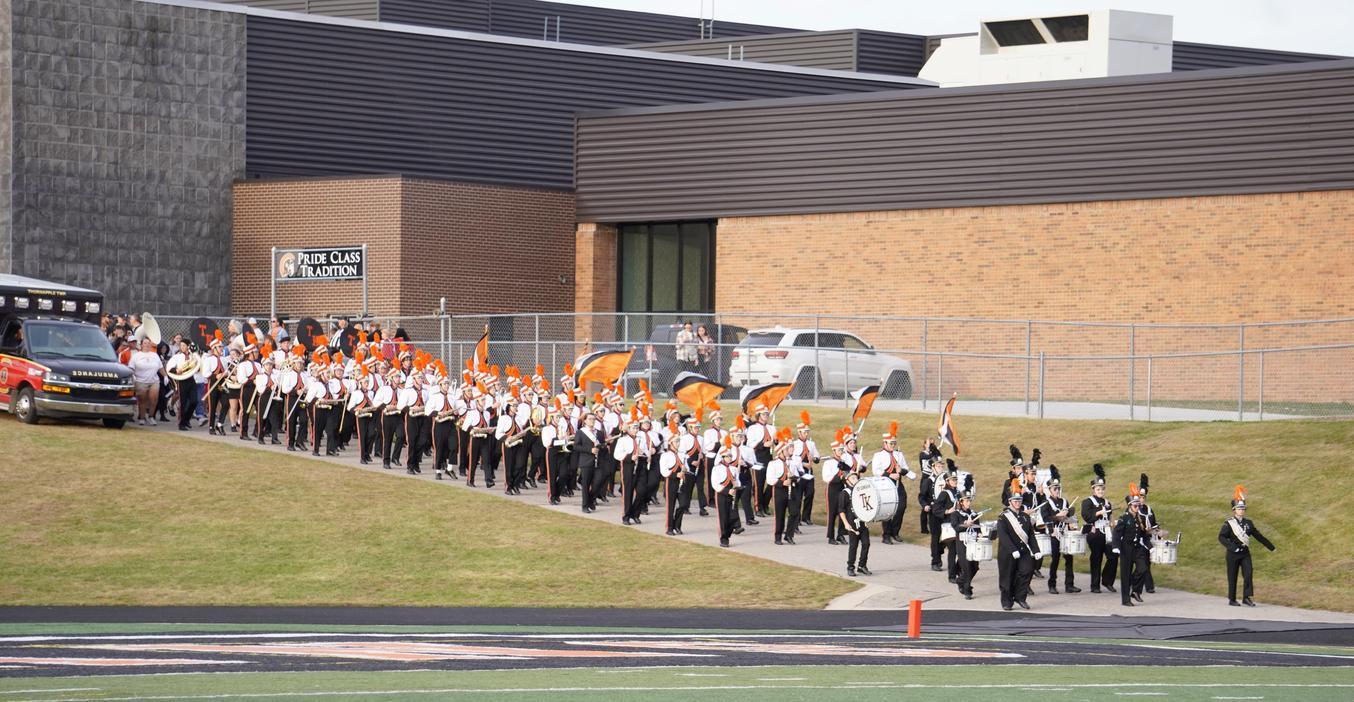 A marching band parades in uniform, holding orange flags outdoors.