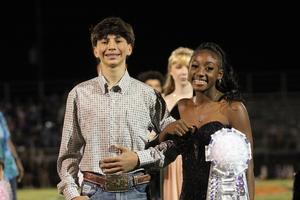 A boy and a girl dressed up, smiling together at an event on a football field.
