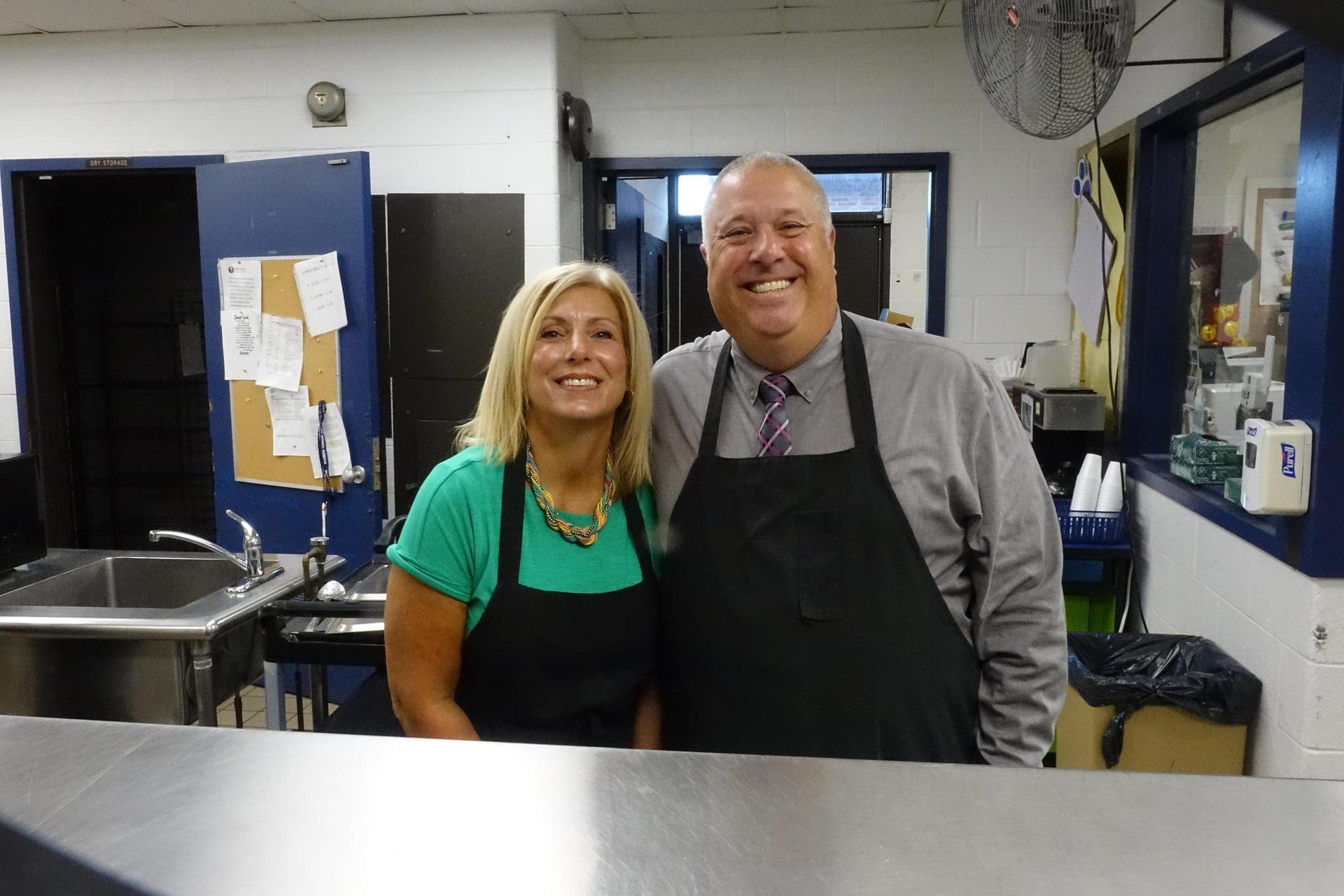 Two cheerful staff members posing in a kitchen environment.