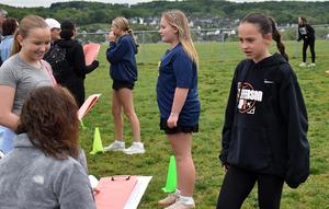 Group of girls and adults conversing during an outdoor event on grass.