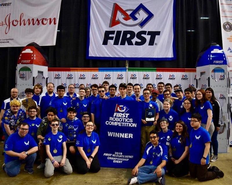 Bensalem High School Robotics Team dressed in royal blue shirts holding a banner naming them Champions