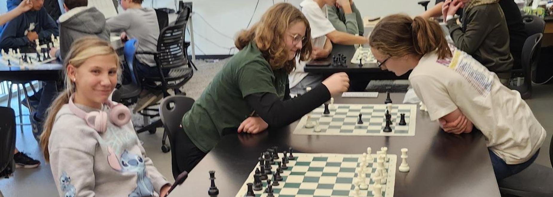A group of young people playing chess at a table in a classroom setting.