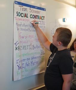 A fifth grade student signs a social contract on the board.