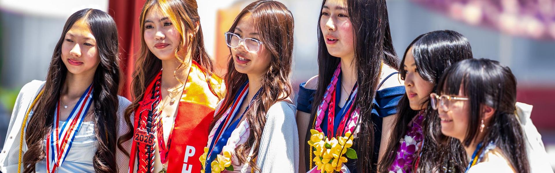 Six young women wearing medals and leis, smiling at an event.
