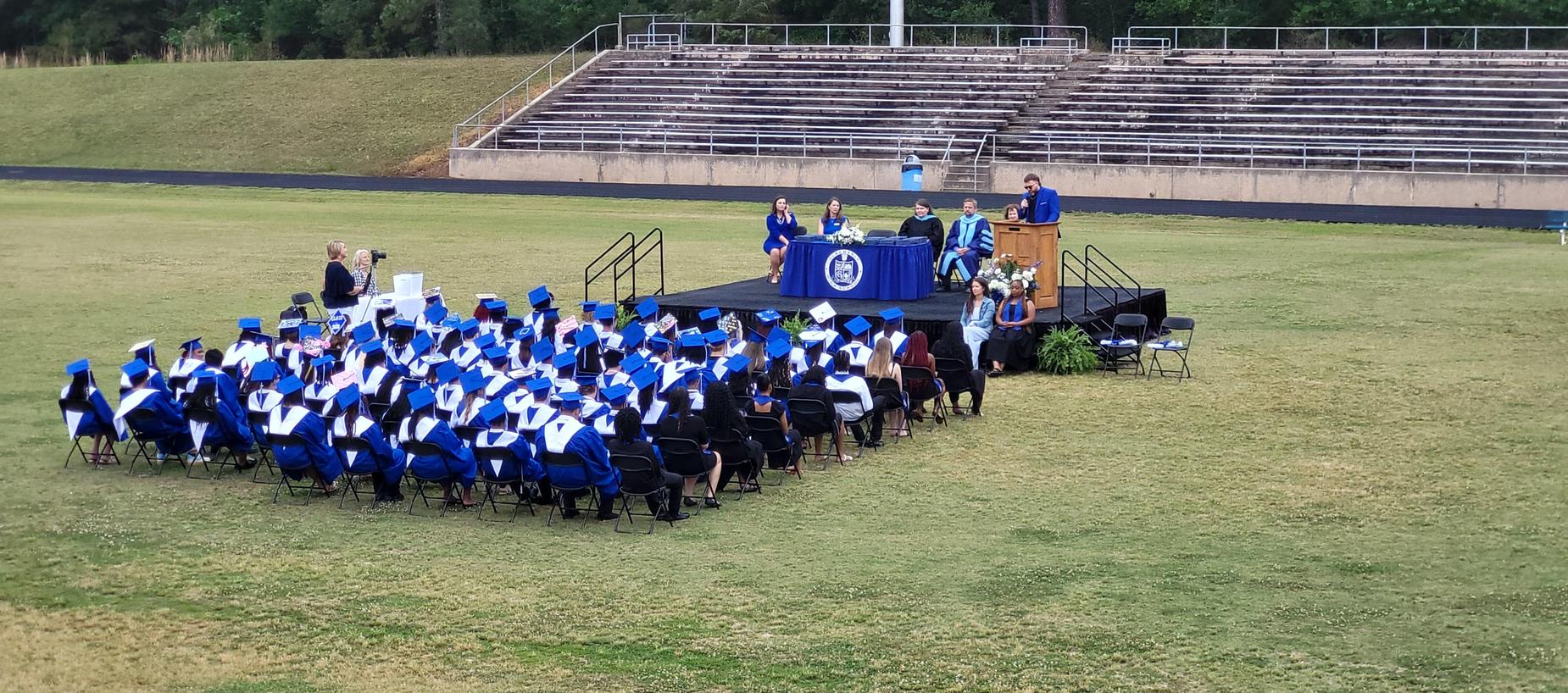A graduation ceremony featuring graduates in caps and gowns seated in front of a stage.
