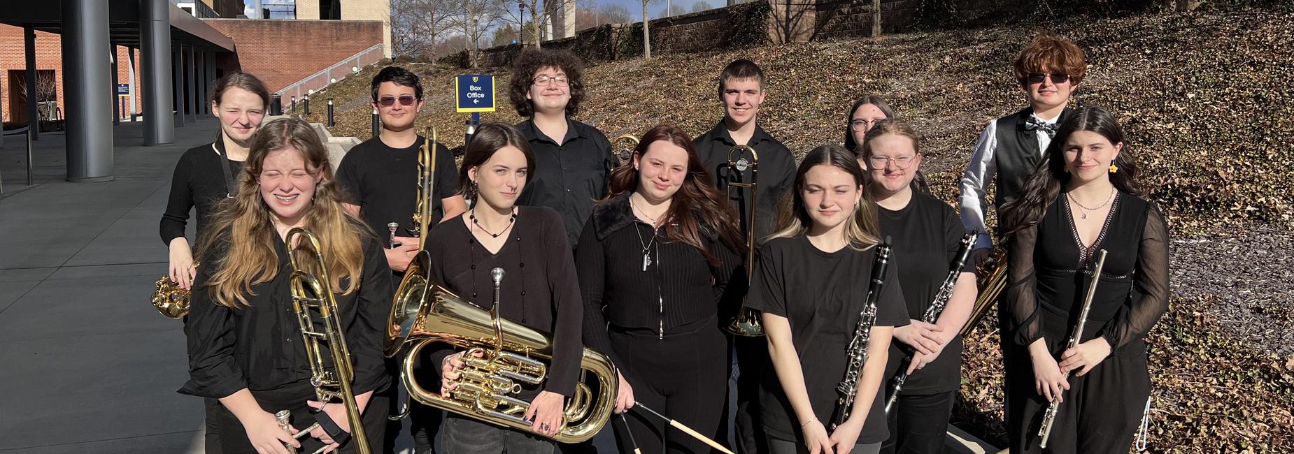 Band students dressed in black standing in two rows posing for picture in front of college sign