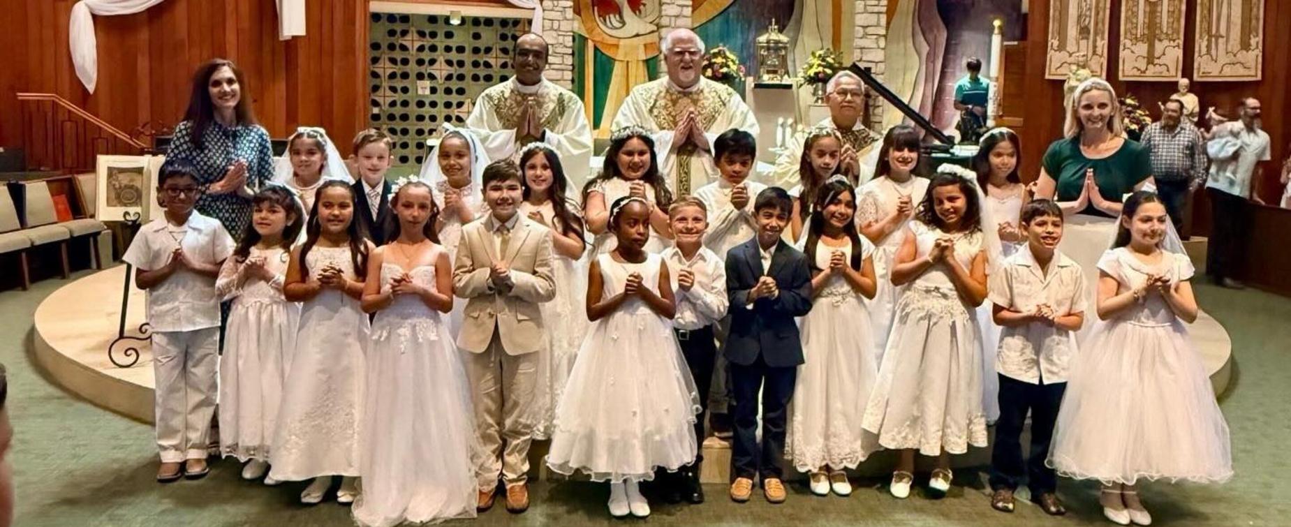 Group of children in white outfits posing with adults in a church setting.