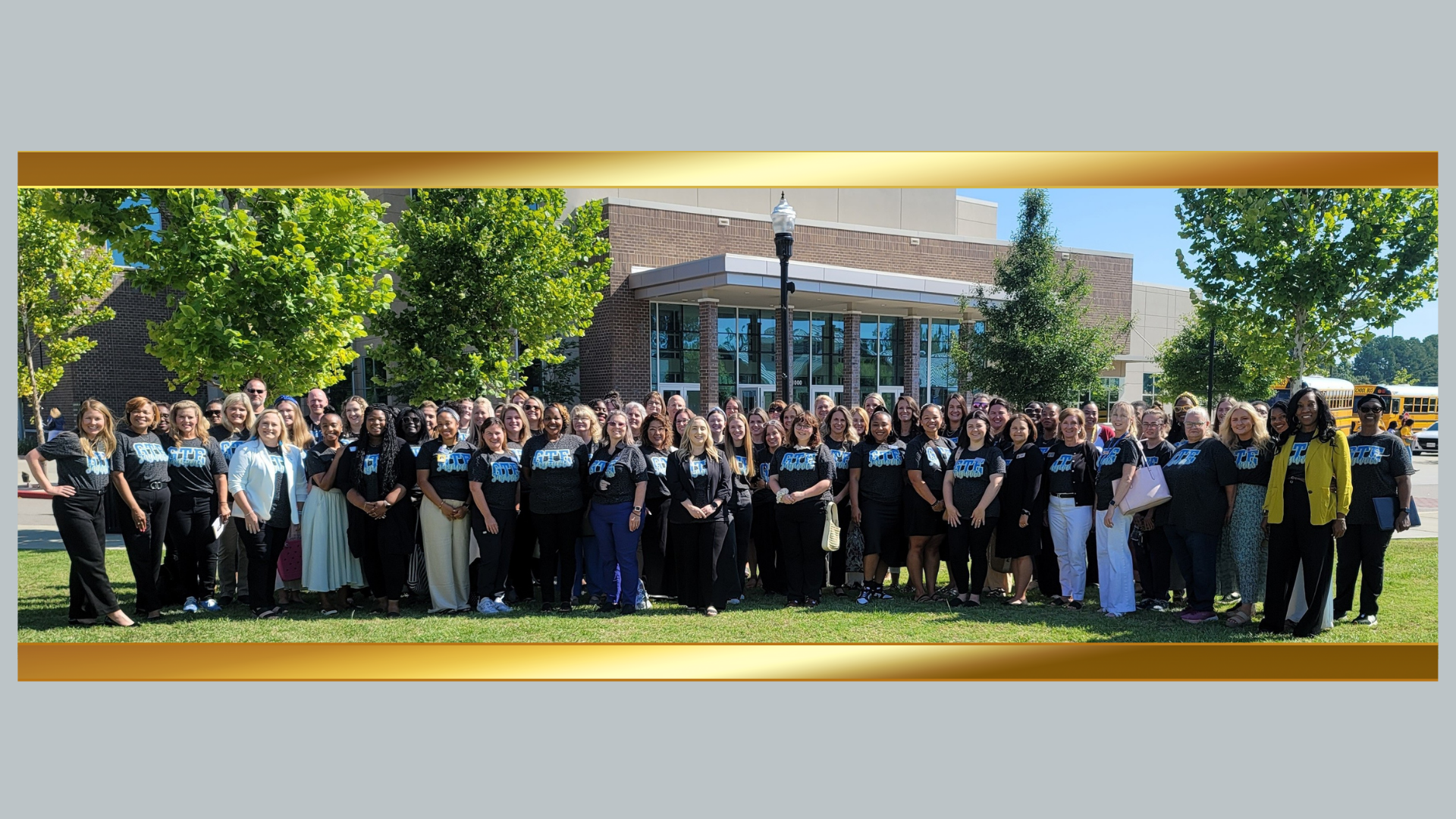 A large staff group photo in front of a school building on a sunny day.