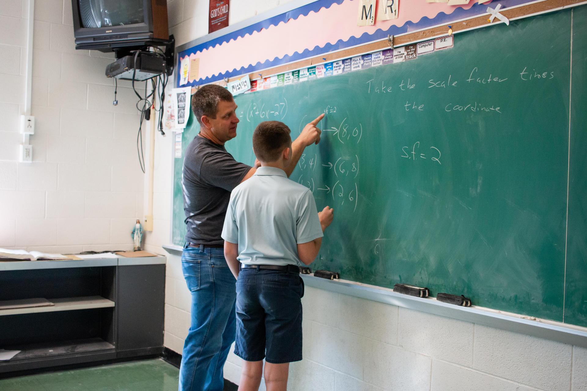 Junior high student being helped by his math teacher at the chalkboard.