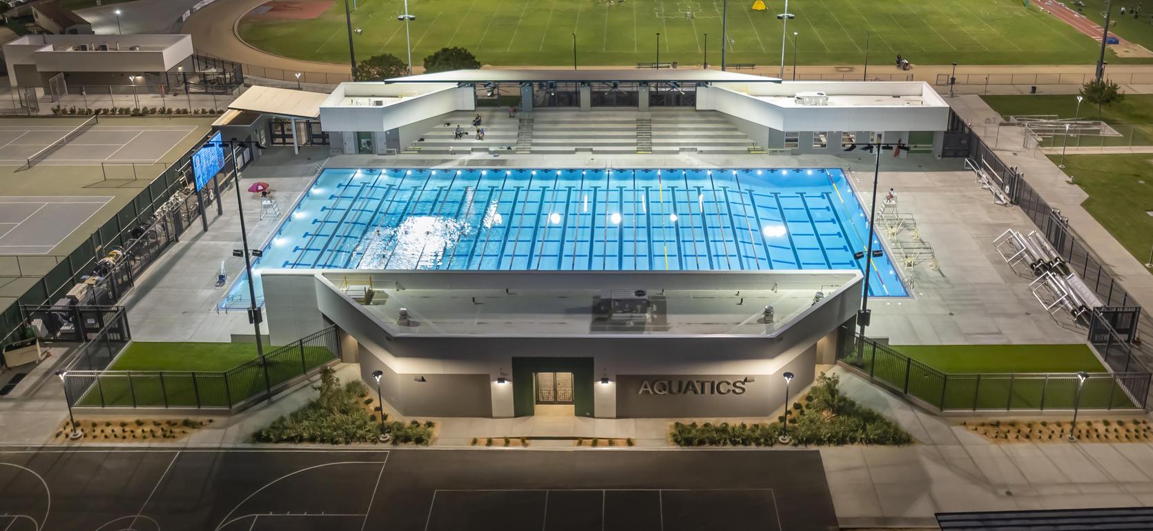 Aerial view of a East Side Aquatic Center and a football field at dusk.