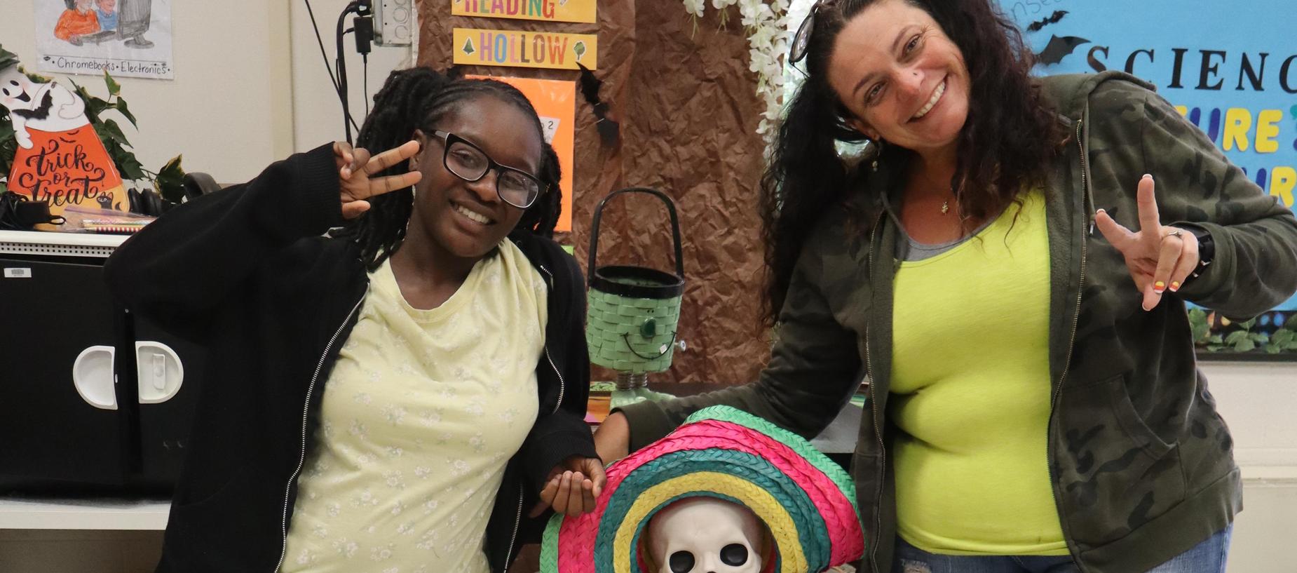 Skeleton in a sombrero and tie sitting in a chair with two people on either side.