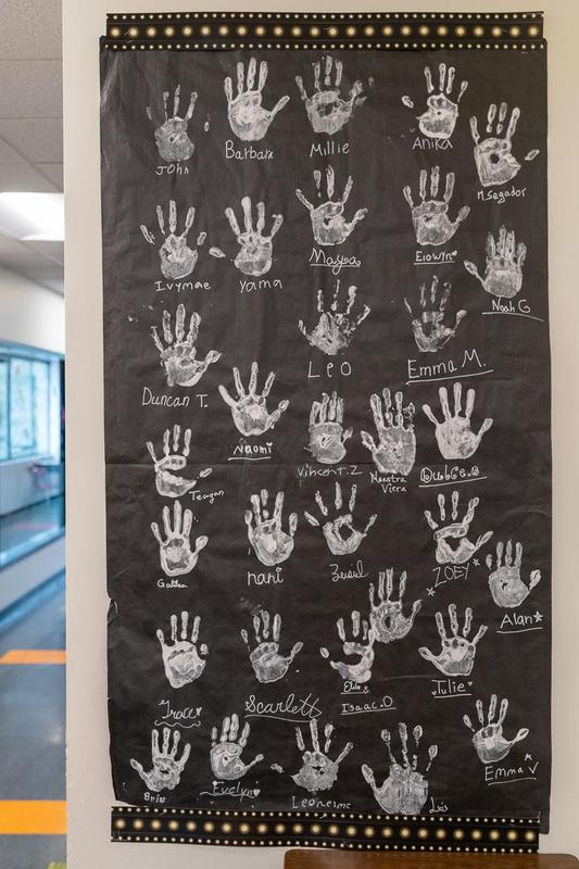 A giant black poster with white handprints of Arco Iris students hangs on a school wall.