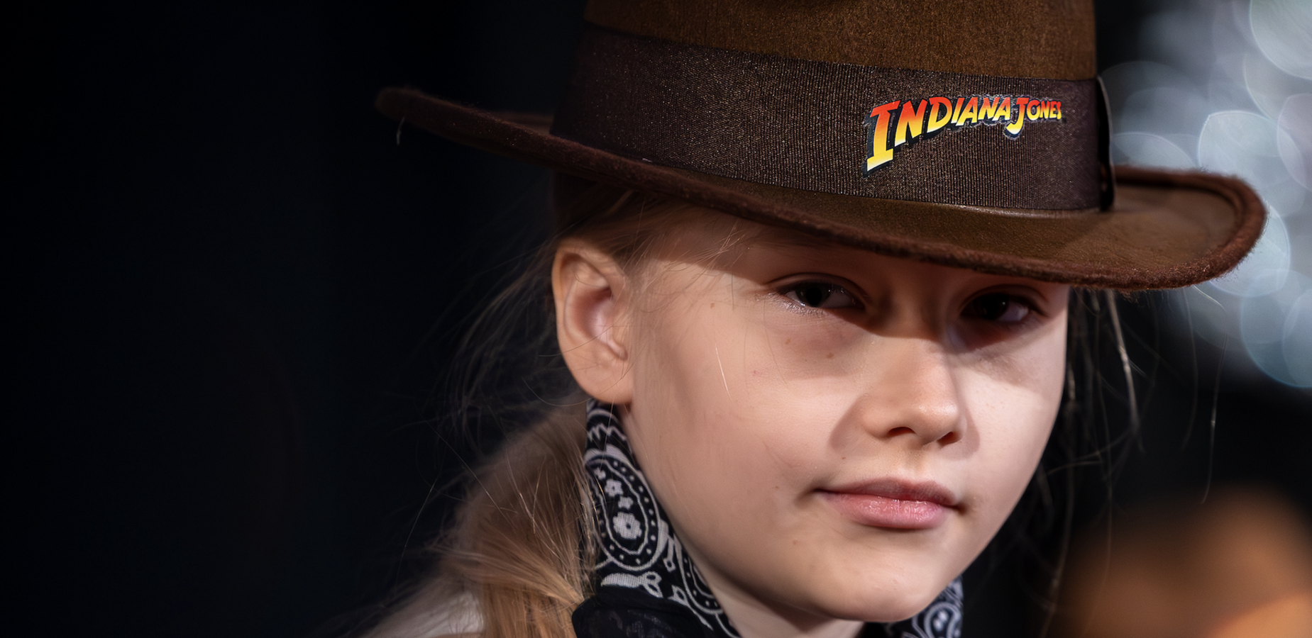 Girl with long hair wearing a cowgirl hat and a black bandana.