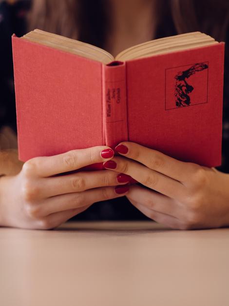 A person with red nails holding a red book open.
