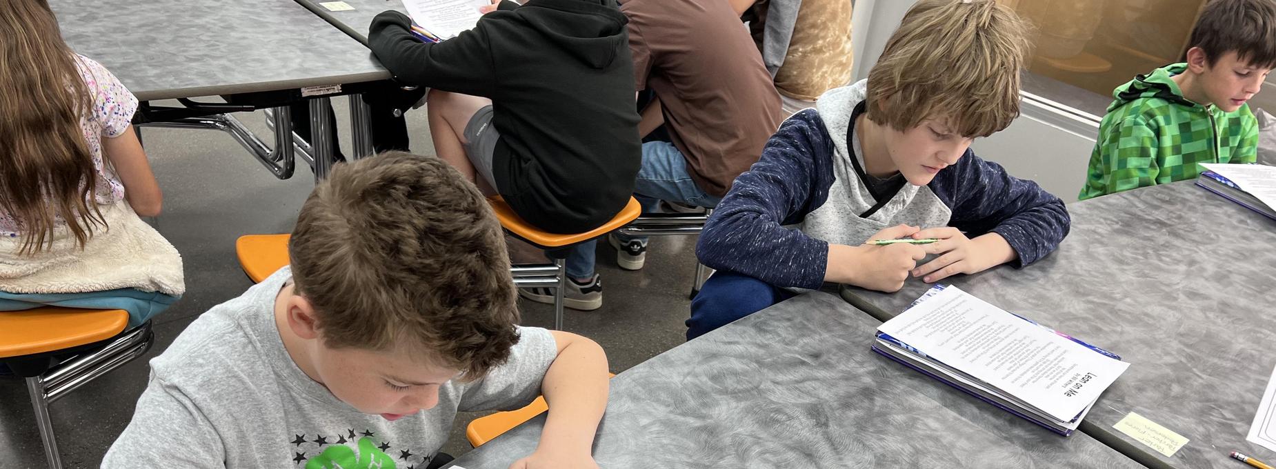 Two boys are focused on their schoolwork at a table in a classroom.