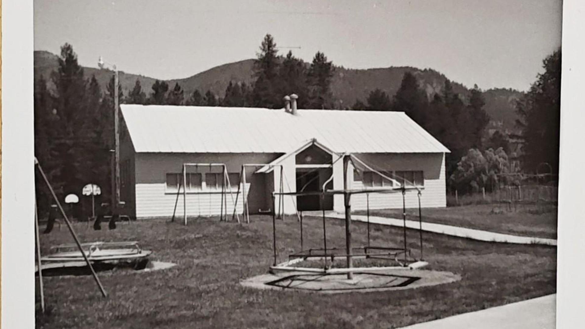 Building with playground equipment in front, mountains in the distance.