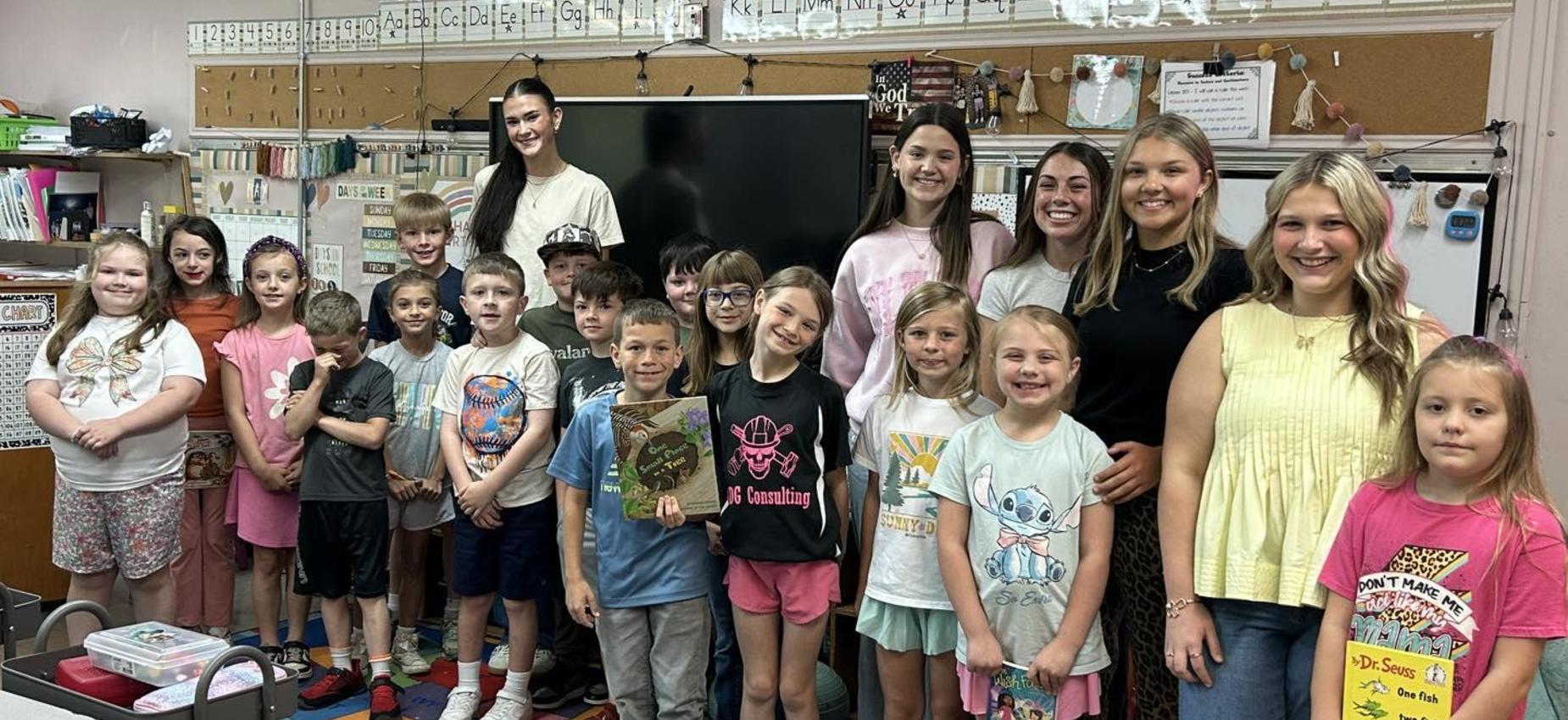 Large group of children and young adults smiling in a classroom.