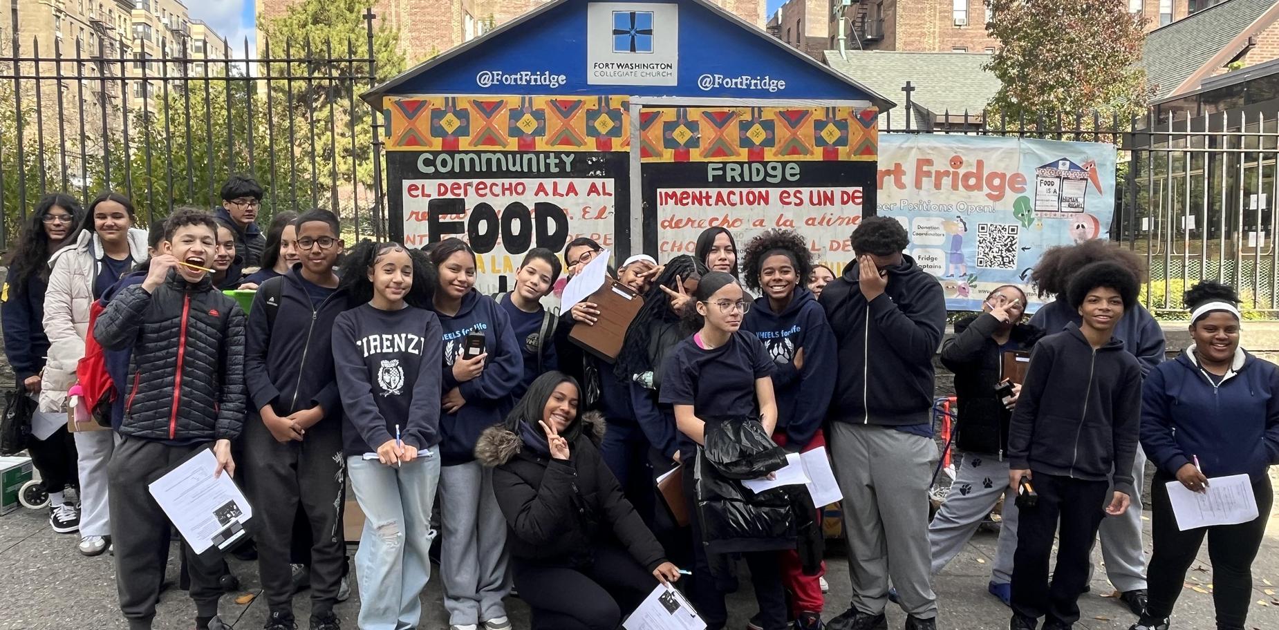 Large group of students posing in front of a community fridge with food resources signage.