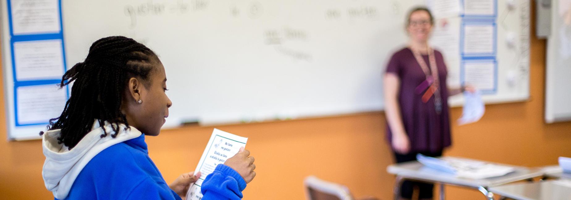Student reads out loud in class as teacher looks on