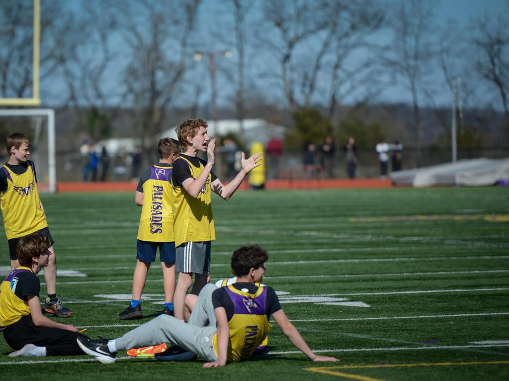 A student athlete and several other players cheering on the football field sidelines.