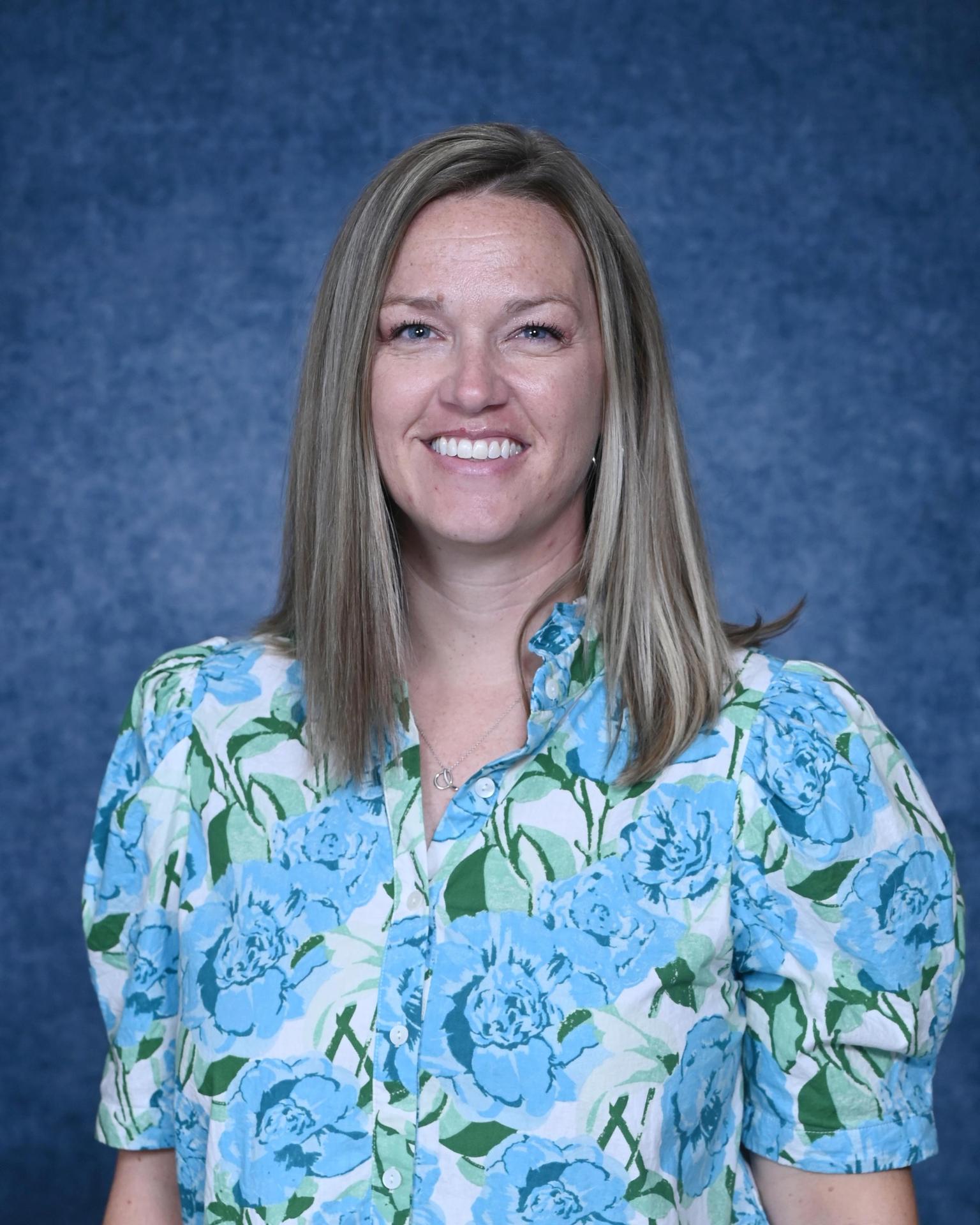 Smiling woman in a colorful patterned shirt against a blue backdrop.