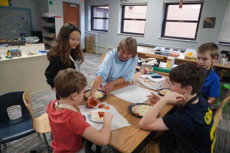 Students work with one of the volunteer grandmothers to make personal pizzas.