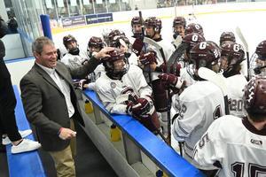 Joel laughing in a sports jacket with his hockey players in their gear at the rink
