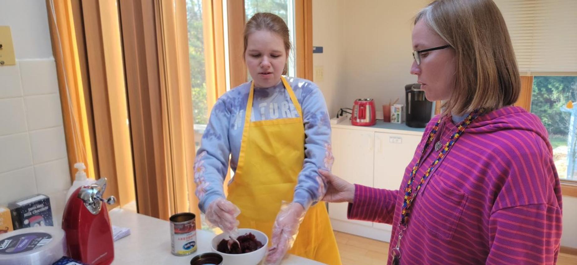 Two people preparing food in a kitchen setting, one wearing an apron.