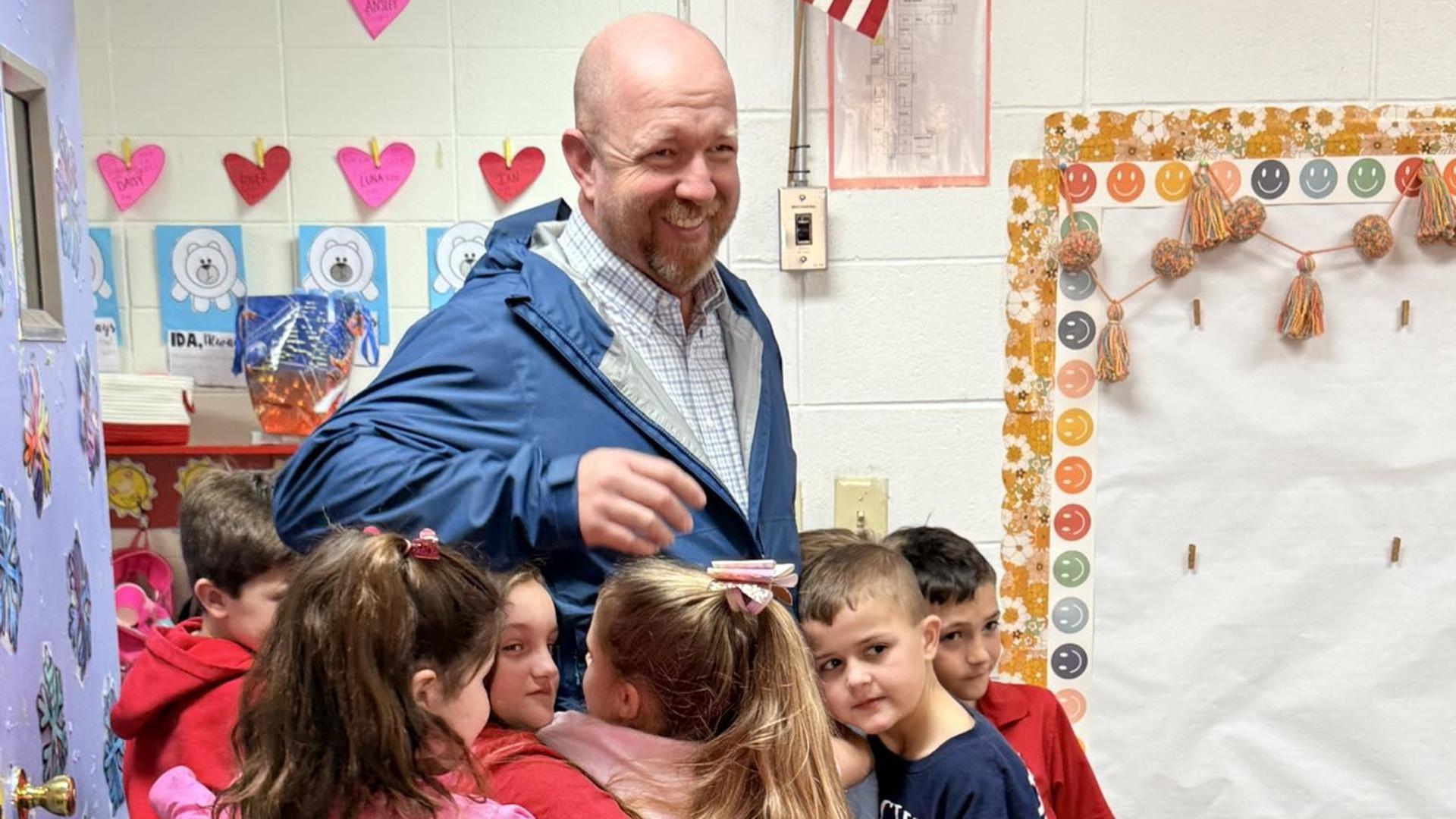 Several children hug a teacher in a classroom setting, showing affection and joy.