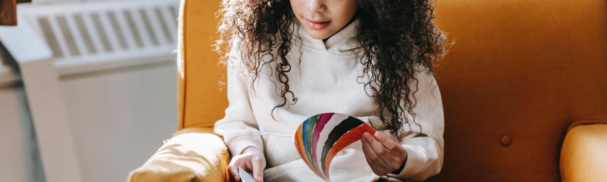 Child with curly hair sitting on a yellow chair, holding a color palette.