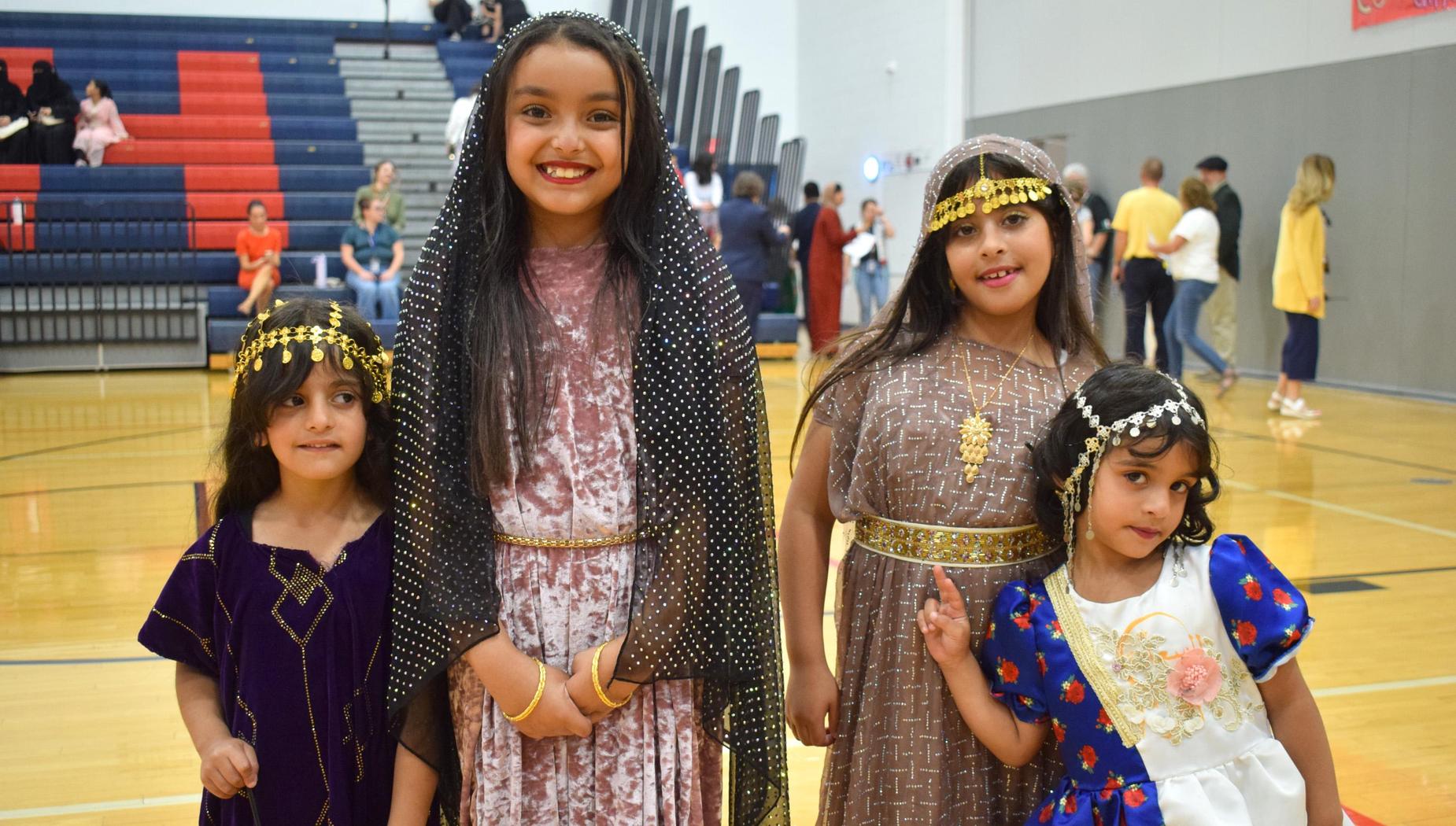Four girls dressed in traditional attire, posing in a gymnasium.