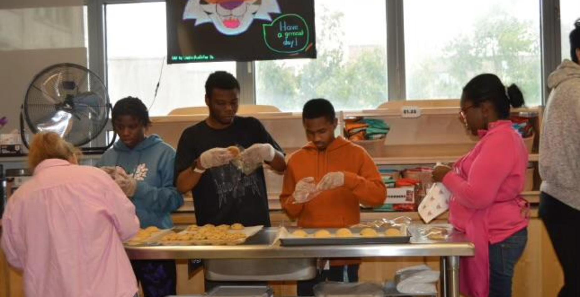 Five students in a kitchen baking cookies together with tools and trays.