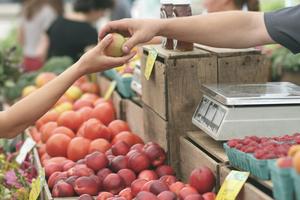 An adult hands someone an apple across a fruit stand.
