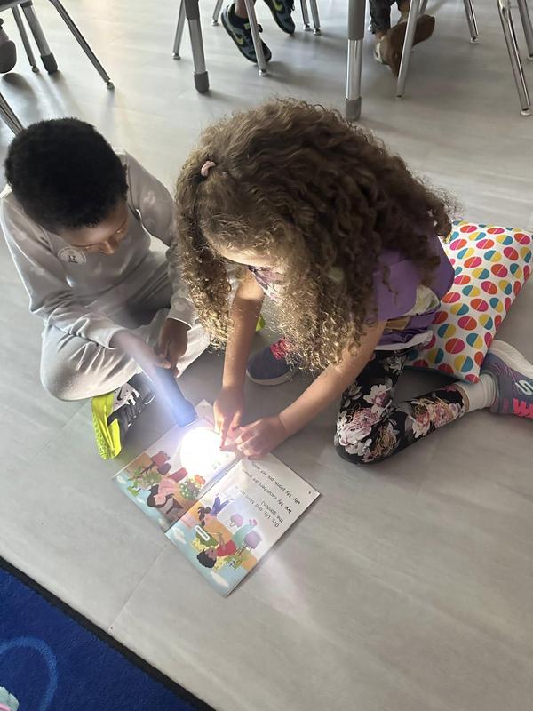 Two children reading a book with a flashlight.