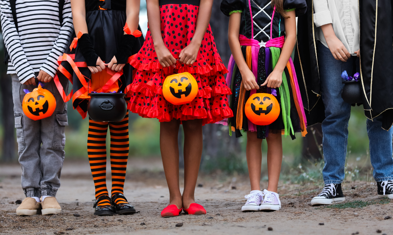 five children in halloween costumes holding their trick or treat bags. No faces shown