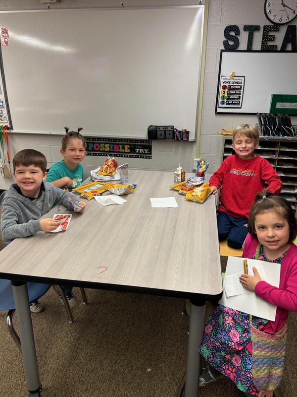 Four children sitting at a table with snacks and drinks.
