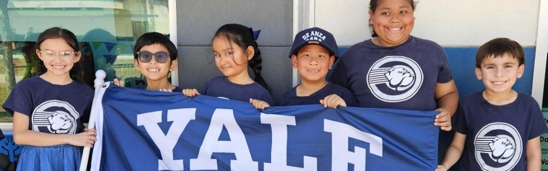 Group of children holding a blue Yale flag, smiling and posing together.