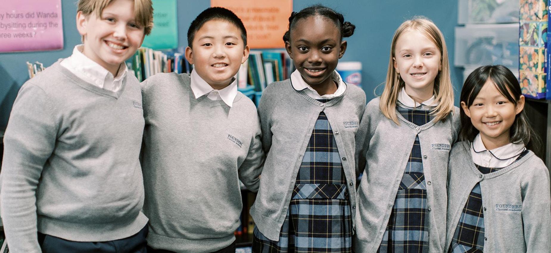 Five smiling elementary students stand together in front of a bookshelf