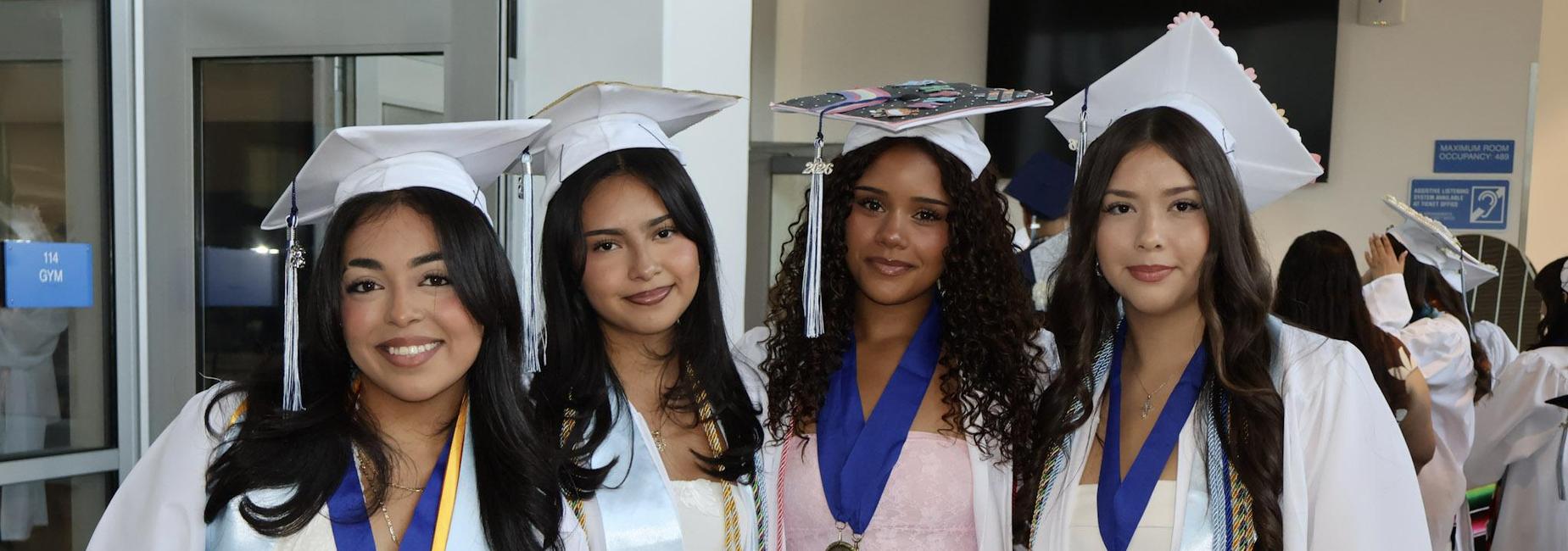 Four graduates in caps and gowns posing together with medals and sashes.