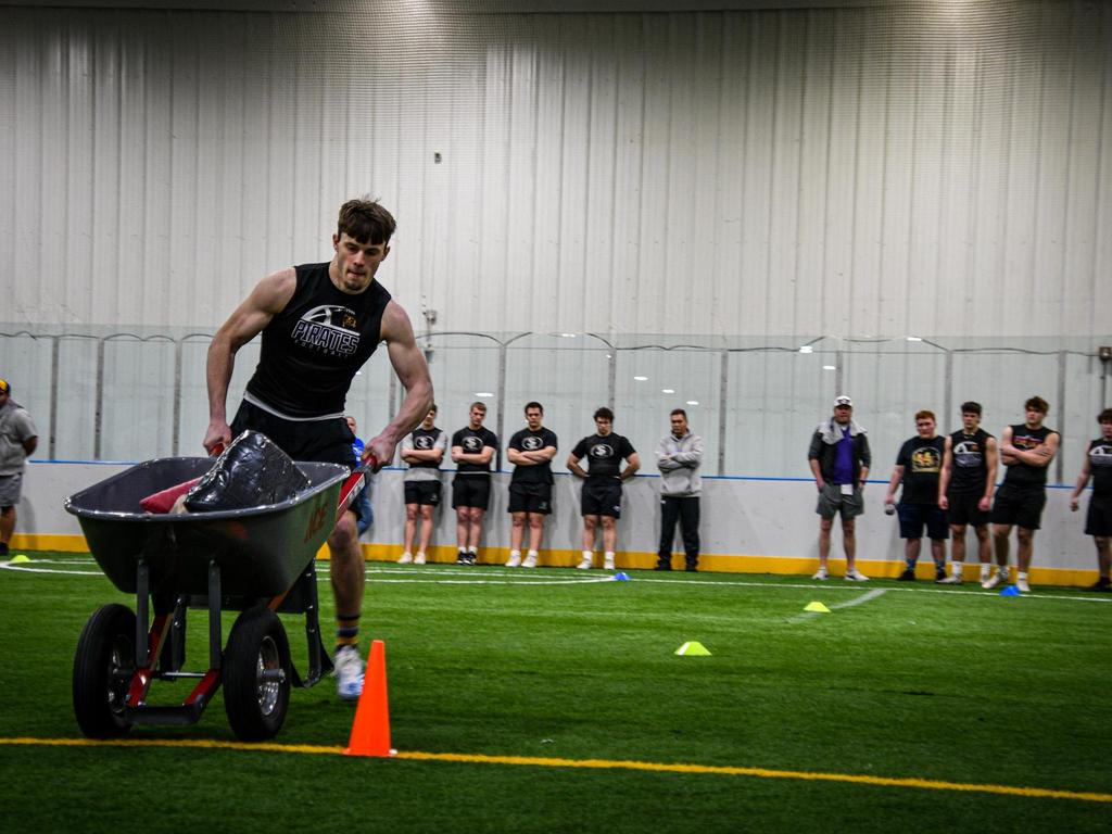 An athlete pushing a wheelbarrow full of heavy items.