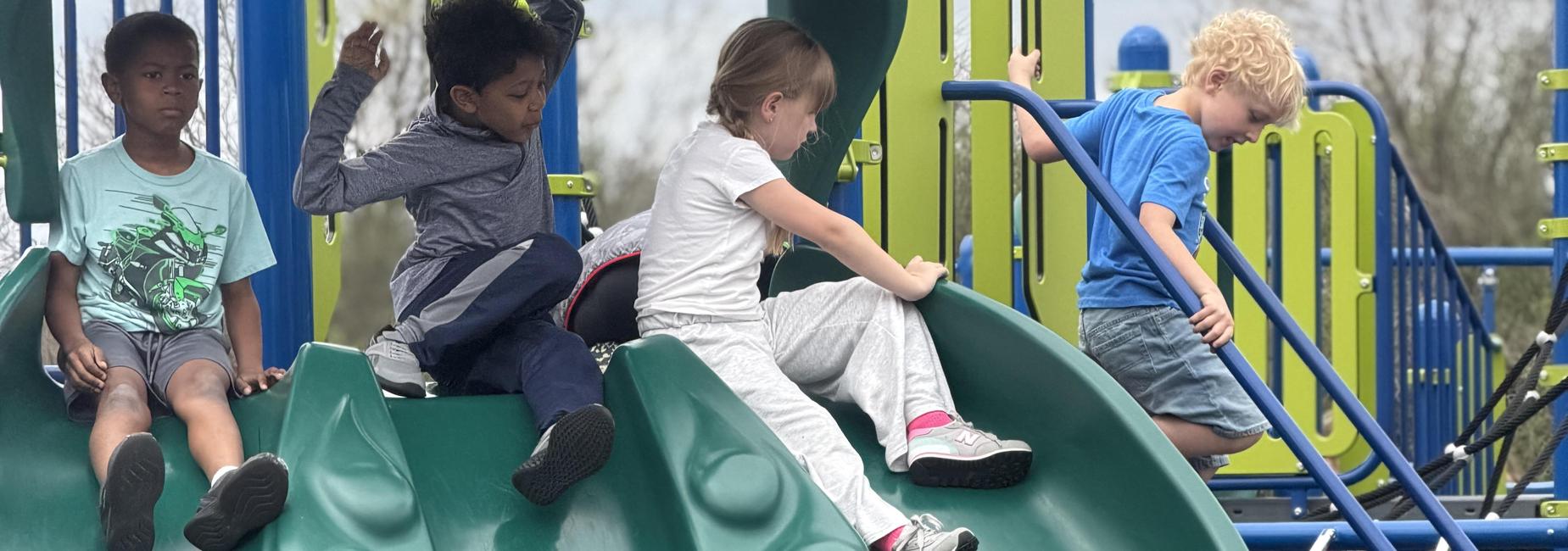 Children playing on a large green slide at a playground.
