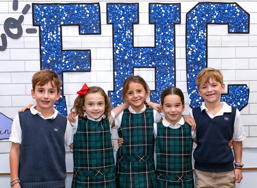 Five children smiling together in matching school uniforms against a sparkly background.