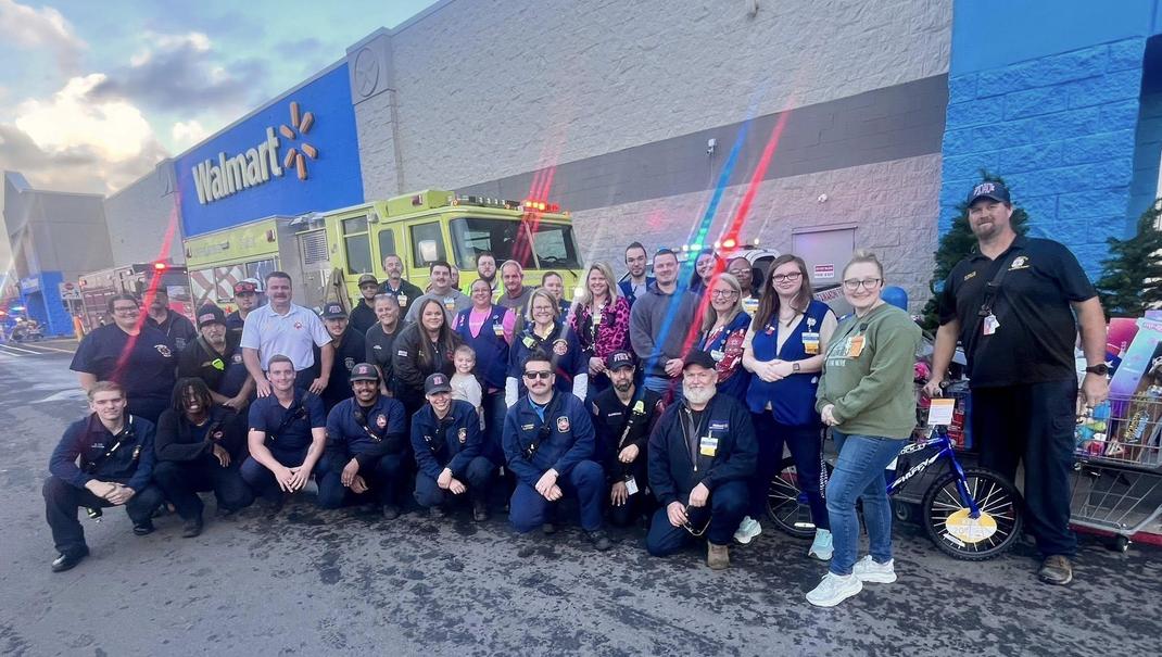 A large group of people, including firefighters and Walmart employees, posing outside a Walmart store.