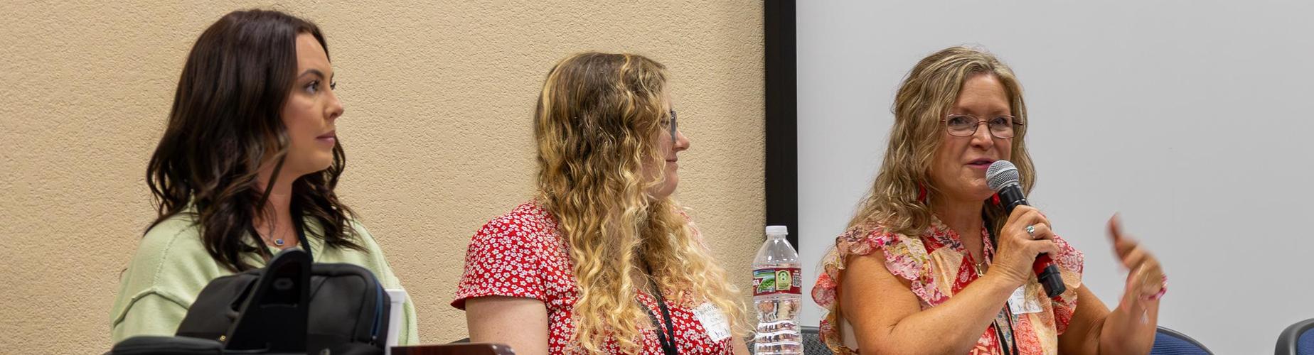Three women speaking at a panel discussion, with microphones and water bottles.
